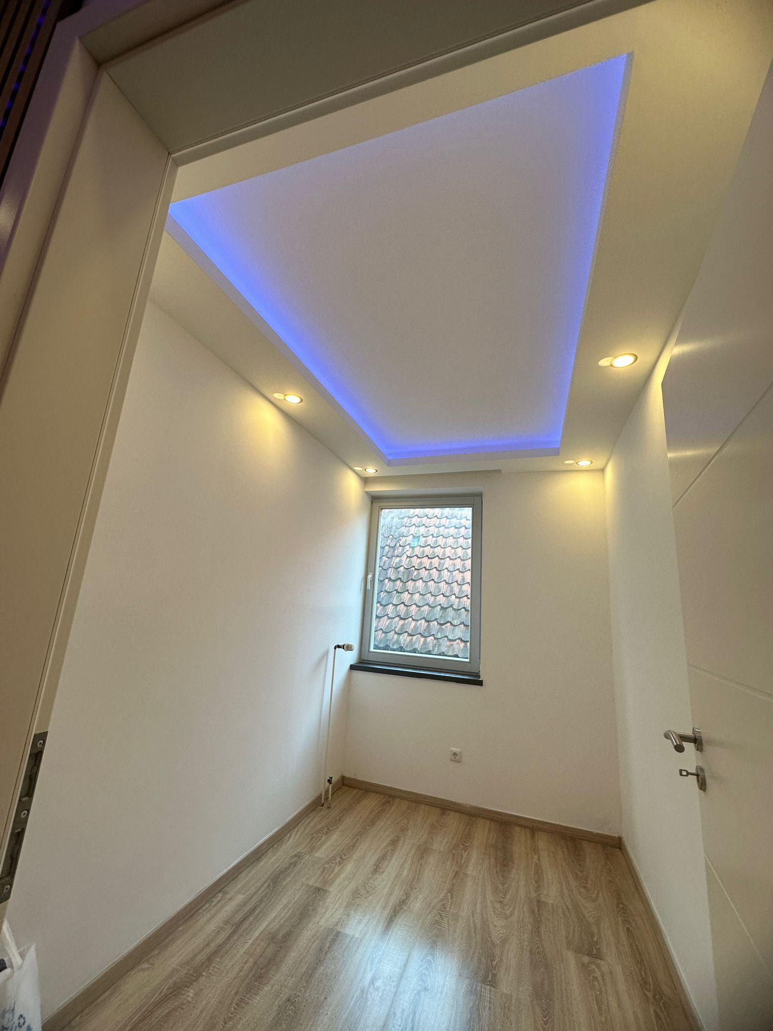 Ein kleiner Raum mit einem Fenster und einem blauen Licht an der Decke.