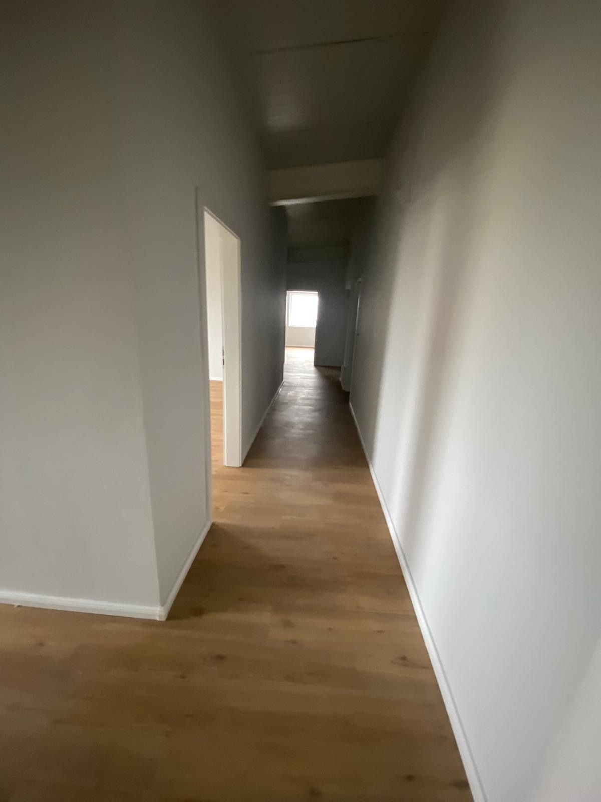 Ein langer Flur mit Holzböden und weißen Wänden in einem Haus.