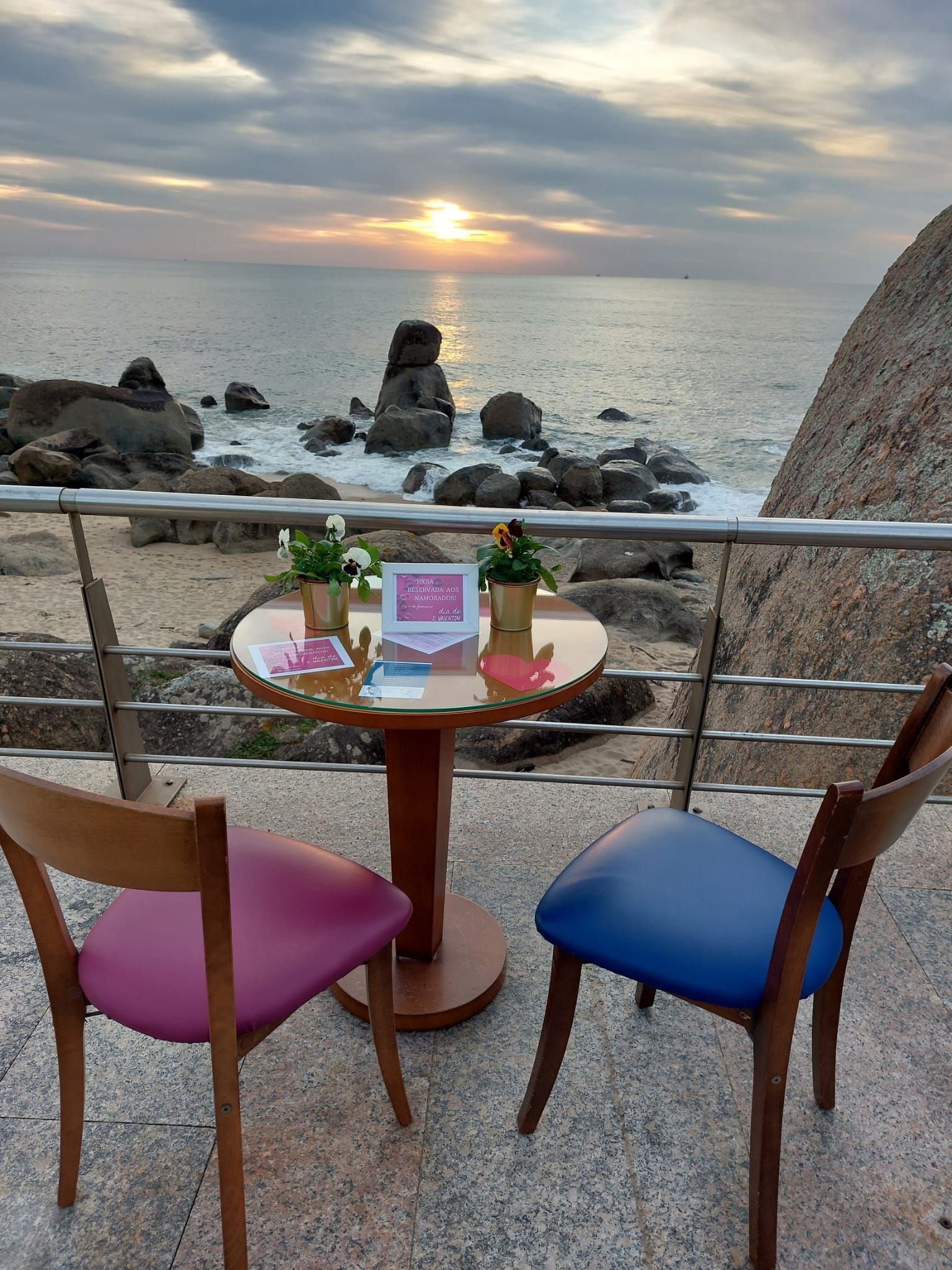Uma mesa e cadeiras em uma varanda com vista para o oceano ao pôr do sol.