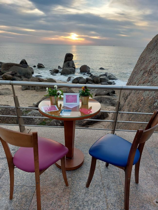 Uma mesa e cadeiras em uma varanda com vista para o oceano ao pôr do sol.