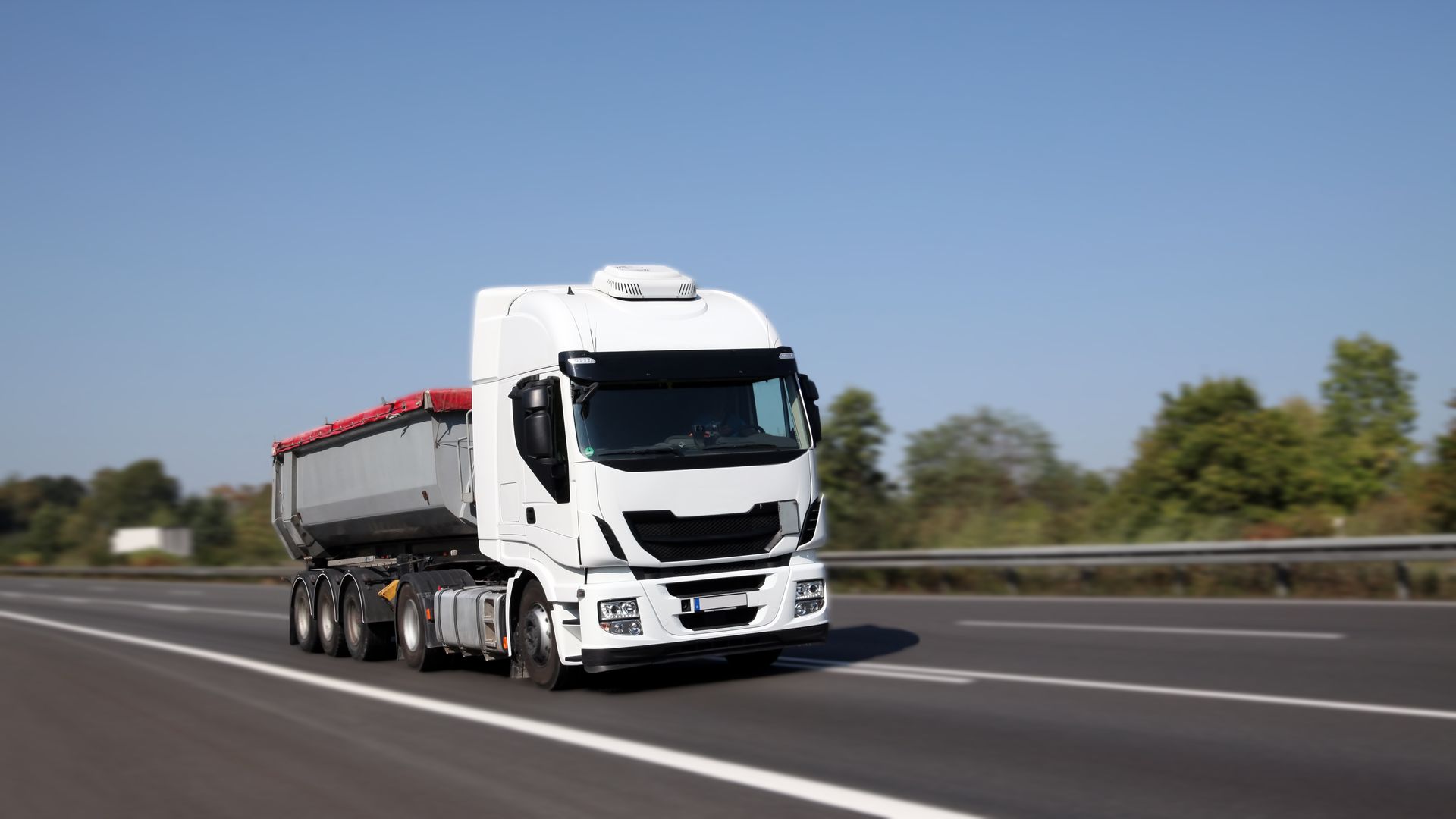 Un camion-benne blanc  sur une autoroute sous un ciel bleu clair