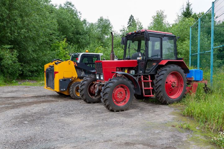Tracteur avec accessoire garé sur du gravier près d'un chemin.