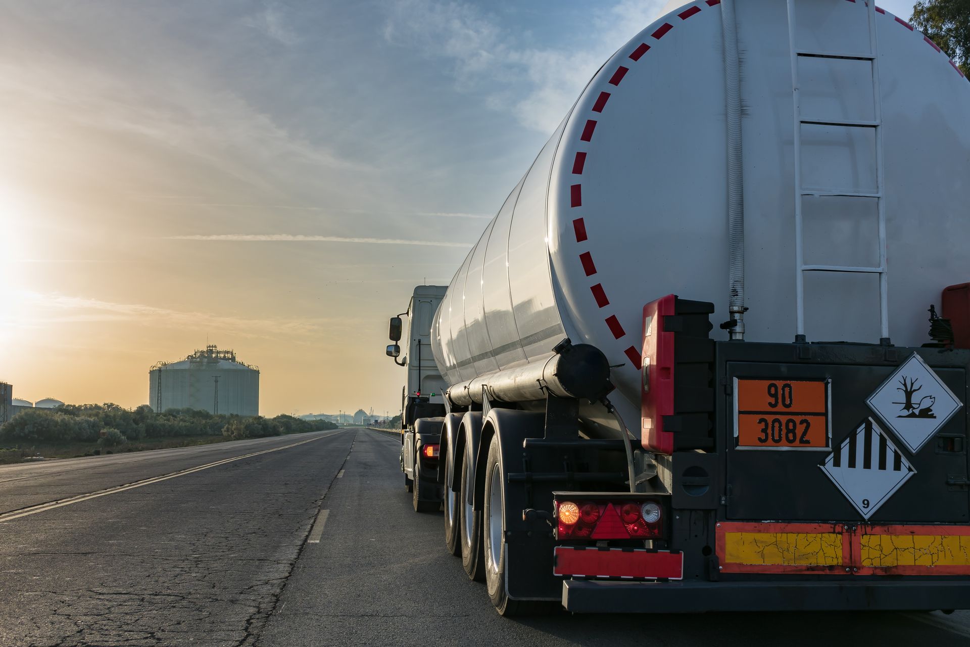 Camion-citerne à carburant sur une autoroute, avec la silhouette d'une ville à l'horizon.