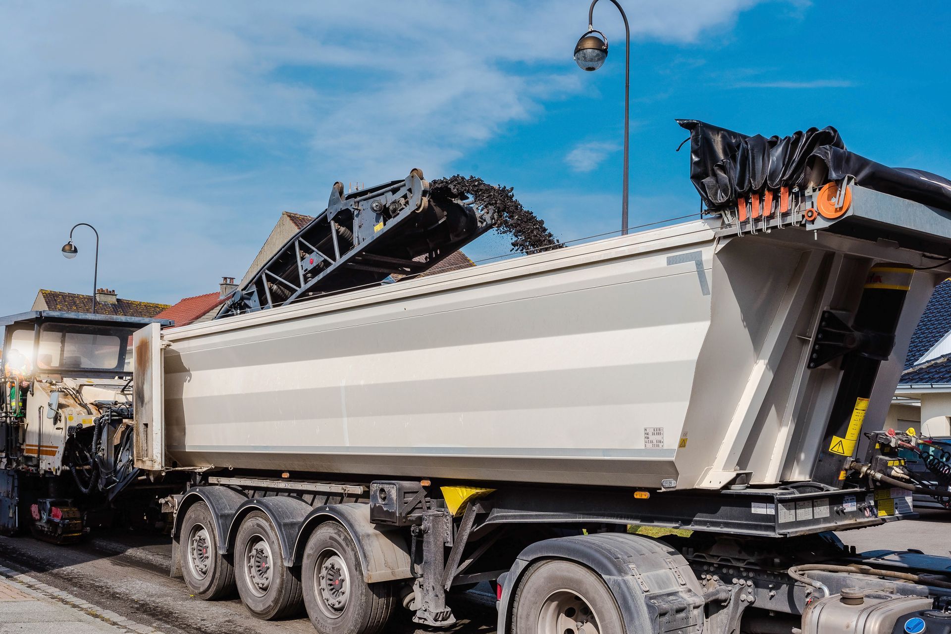Un gros camion-benne décharge de l'asphalte noir sous un ciel bleu sur un chantier de construction