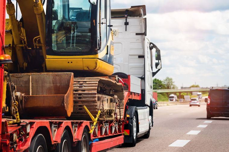Une pelleteuse sur une remorque, garée à côté d'un camion sur une autoroute.