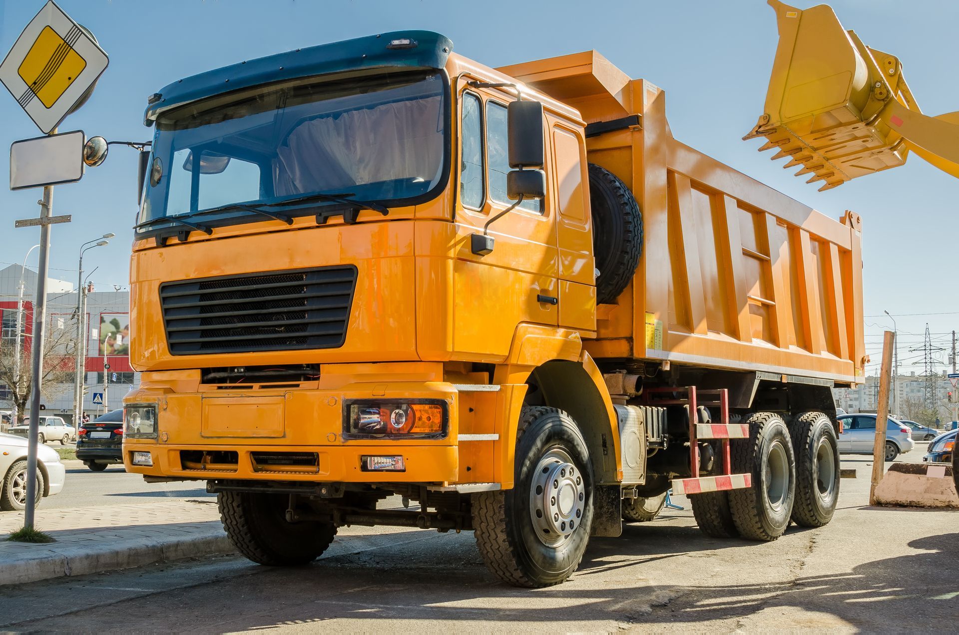 Camion-benne orange sur un chantier de construction, avec une benne surélevée et un bras d'excavatrice à proximité