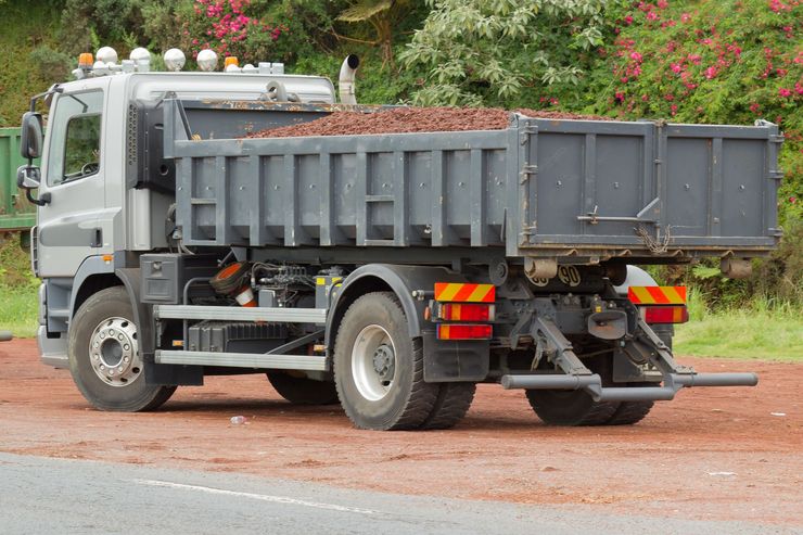 Un camion-benne est stationné sur un chemin de terre, avec des fleurs.