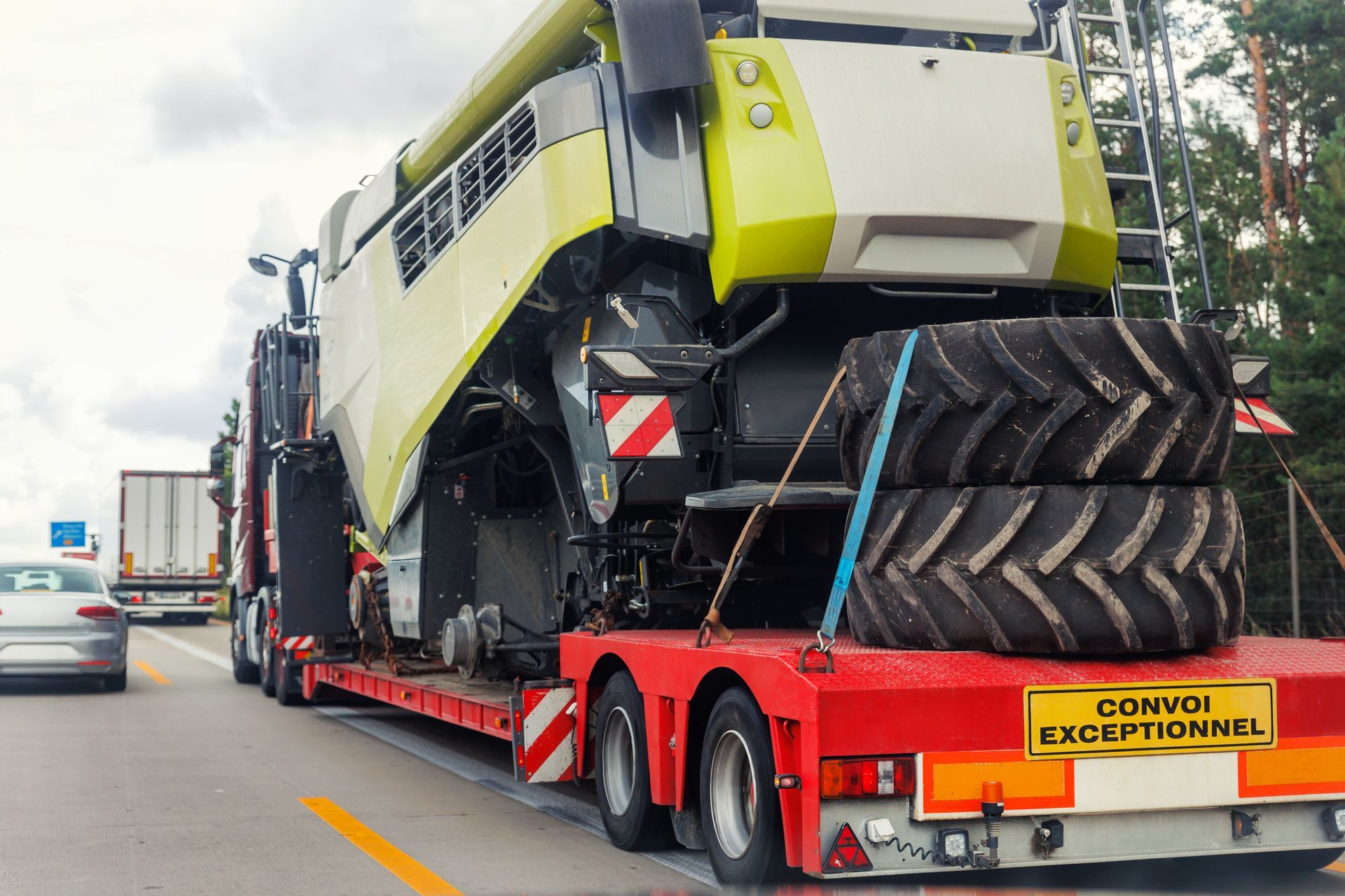 Une grosse machine agricole est fixée sur une remorque plateau et circule sur une autoroute.