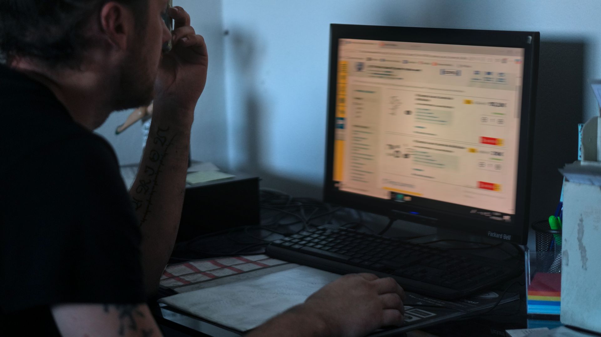 Un mécanicien en salopette bleue utilise un téléphone et une lampe de poche pour inspecter le moteur d'une voiture dans un garage.