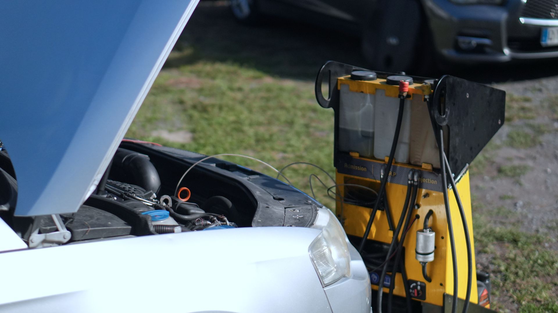 Mécanicien en uniforme bleu utilisant une tablette lors de l'inspection d'un moteur de voiture dans un garage.