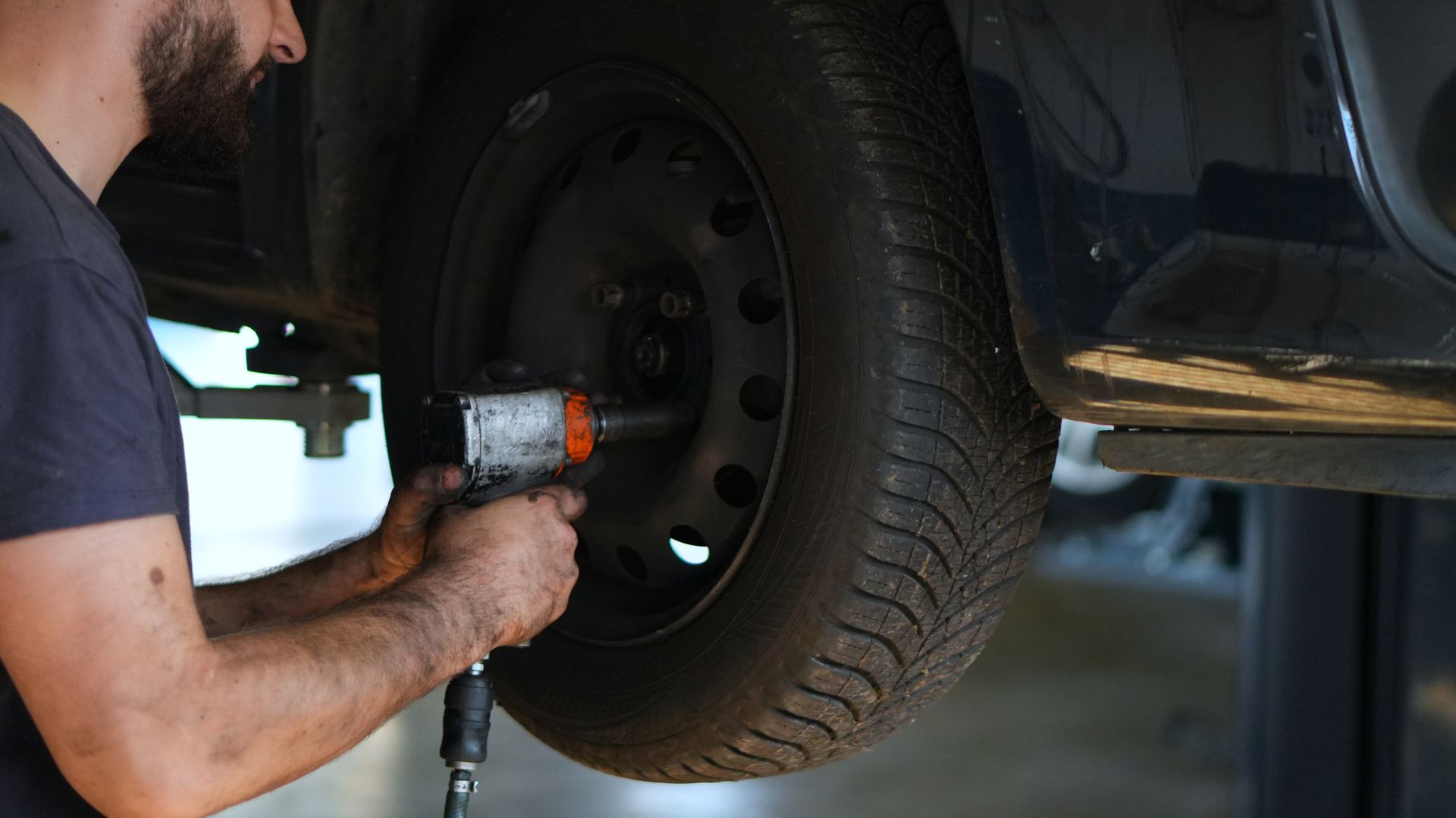 Mécanicien en gants noirs travaillant sur un disque de frein et un étrier de voiture dans un garage.