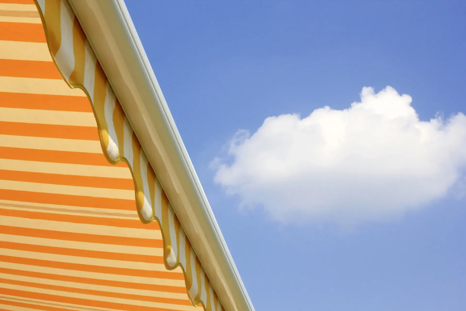 Toldo de rayas naranjas y blancas contra un cielo azul con una nube blanca.
