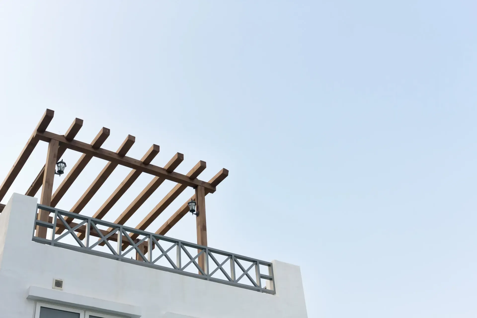 Edificio blanco con una pérgola de madera en el techo contra un cielo azul claro.