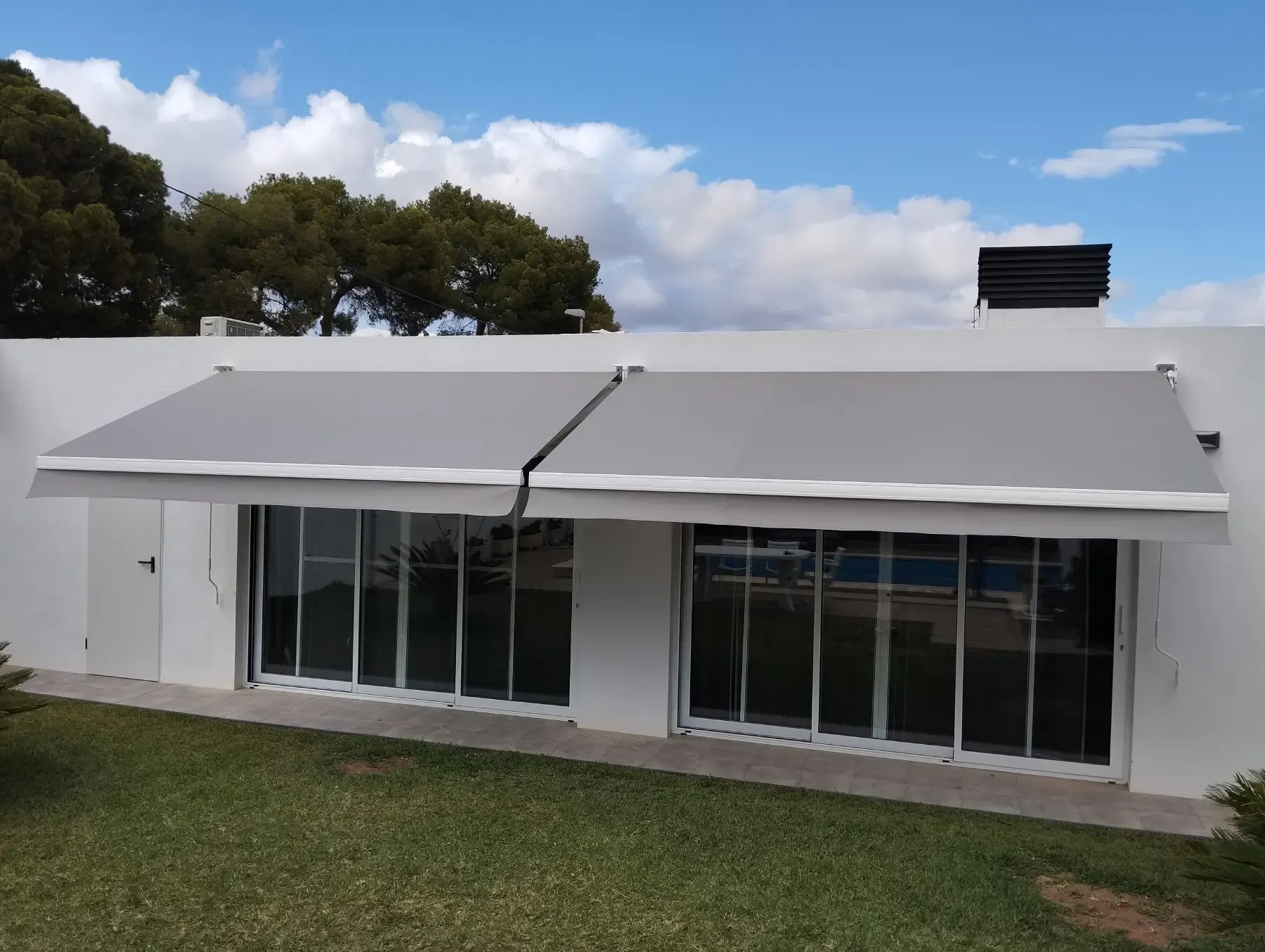 Toldo retráctil de color gris oscuro con marco blanco fijado a una estructura de madera.