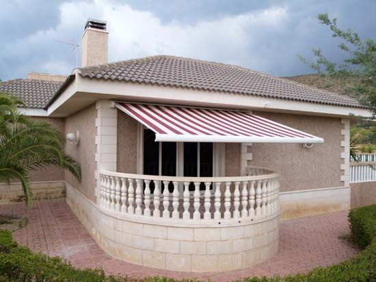Casa con balcón y toldo de rayas que se extiende sobre un conjunto de puertas de vidrio.