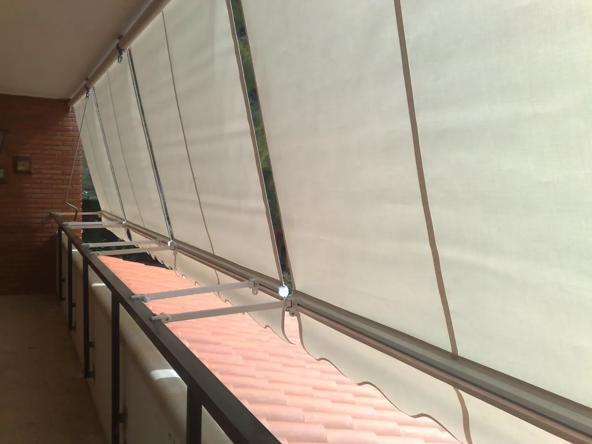 Un toldo amarillo en un balcón sombrea parcialmente la zona. Al fondo se ve un edificio y una zona verde.