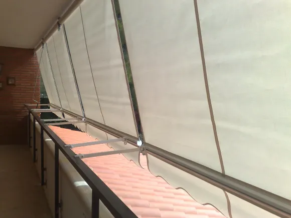 Un toldo amarillo en un balcón sombrea parcialmente la zona. Al fondo se ve un edificio y una zona verde.