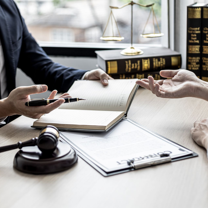 Un avocat examine des documents avec un client à un bureau, marteau et balance visibles.