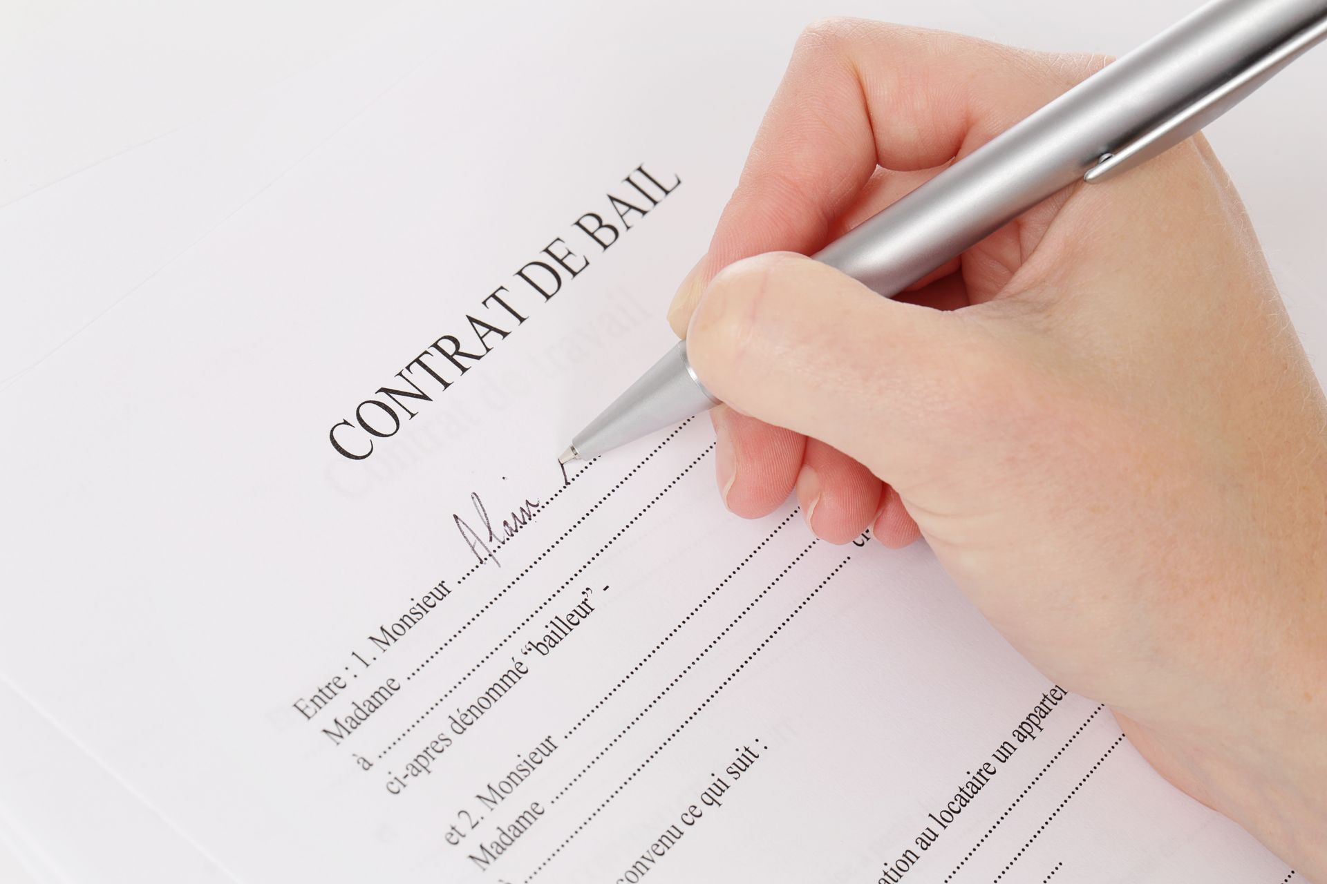 Signature à la main d'un CONTRAT DE BAIL (contrat de location) avec un stylo argenté sur du papier blanc.