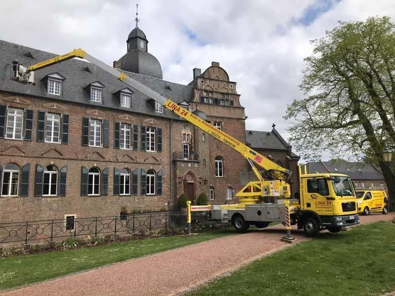 Ein gelber Lastwagen mit einem daran befestigten Kran steht vor einem großen Gebäude.
