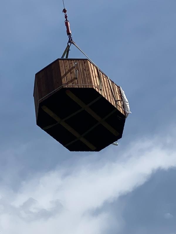Eine große Holzkiste wird von einem Kran in die Luft gehoben