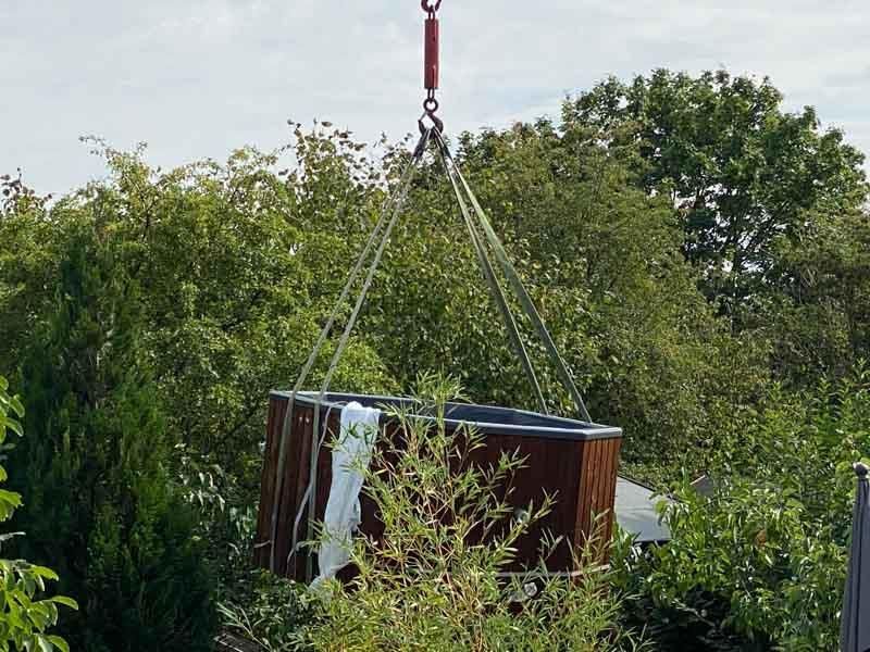 Ein Whirlpool wird von einem Kran in einen Garten gehoben.