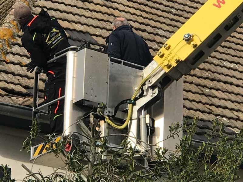 Zwei Männer arbeiten auf einem Dach mit einem gelben Kran mit dem Buchstaben W darauf