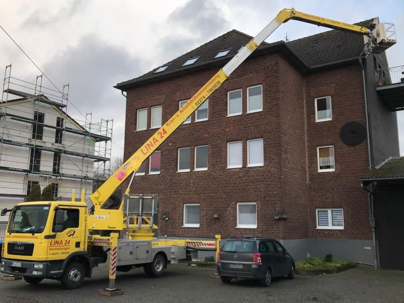 Ein gelber LKW mit einem daran befestigten Kran steht vor einem Backsteingebäude