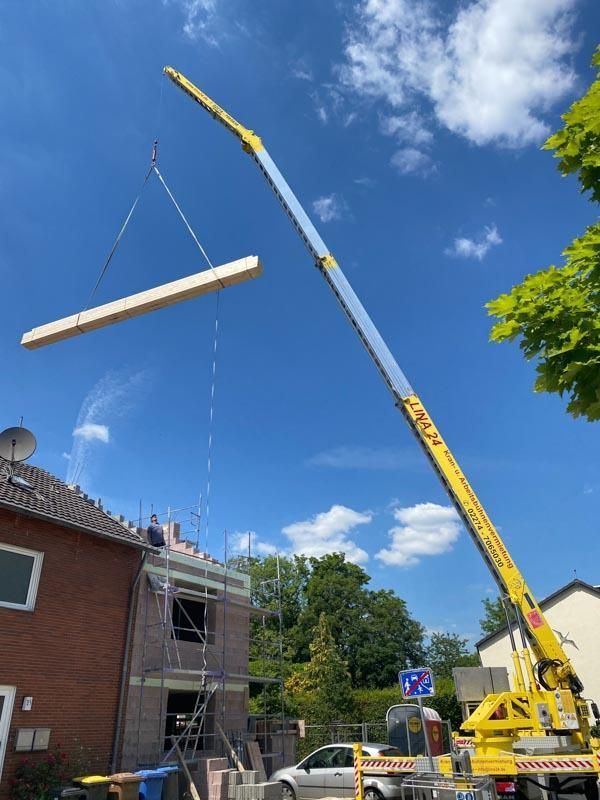 Ein gelber Kran hebt ein Stück Holz über ein Haus