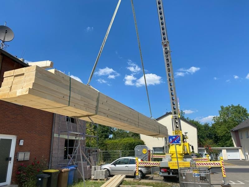 Ein gelber Kran hebt ein großes Stück Holz