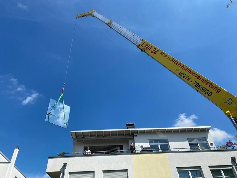 Ein gelber Kran hebt ein großes Stück Glas