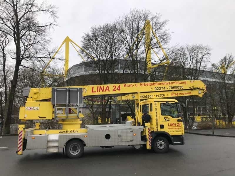 Ein gelber Lastwagen mit einem Kran auf der Ladefläche steht am Straßenrand.