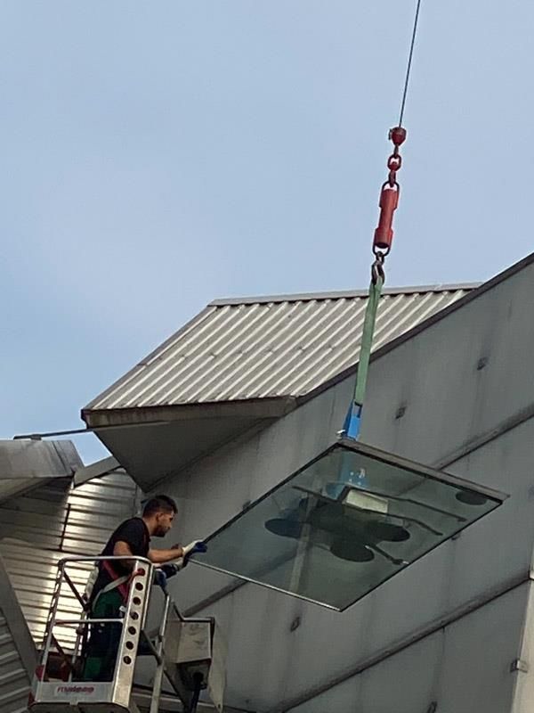 Ein Mann steht auf einer Leiter, während ein Kran eine Glasscheibe vom Dach eines Gebäudes hebt.