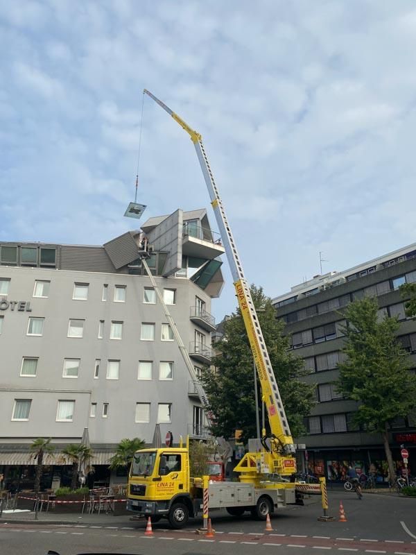 Ein gelber LKW mit einem daran befestigten Kran steht vor einem Hotel