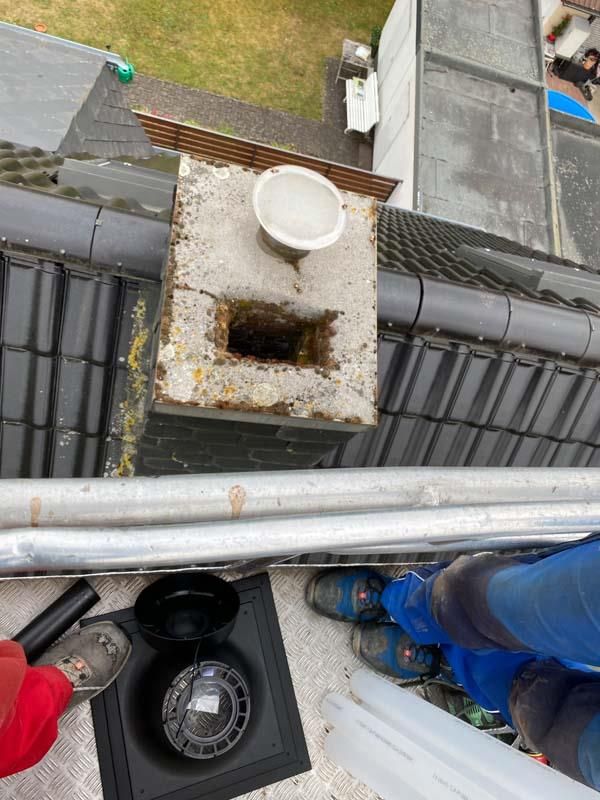 Ein Mann arbeitet an einem Schornstein auf dem Dach eines Hauses.