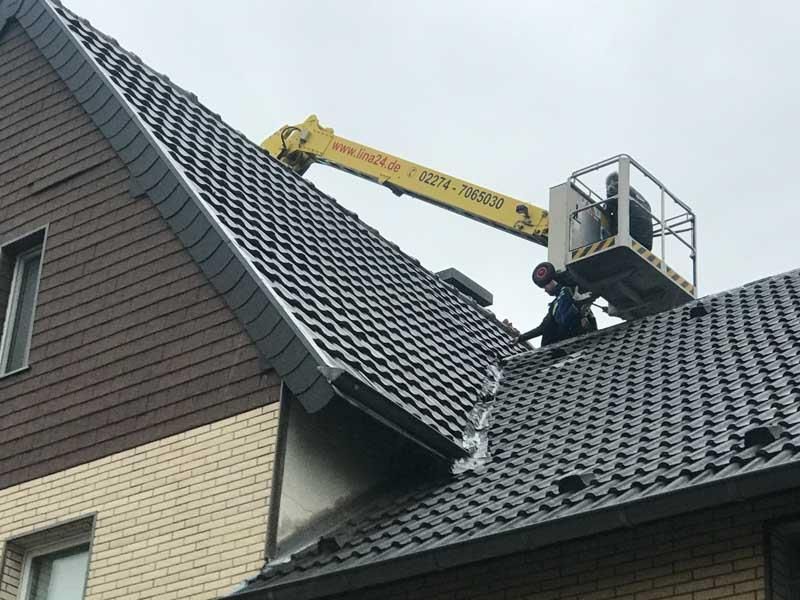 Ein Mann arbeitet mit einem Kran auf dem Dach eines Hauses.