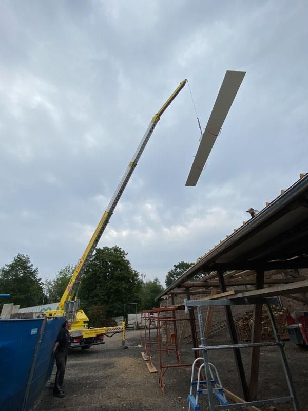 Ein gelber Kran hebt ein Stück Holz in die Luft