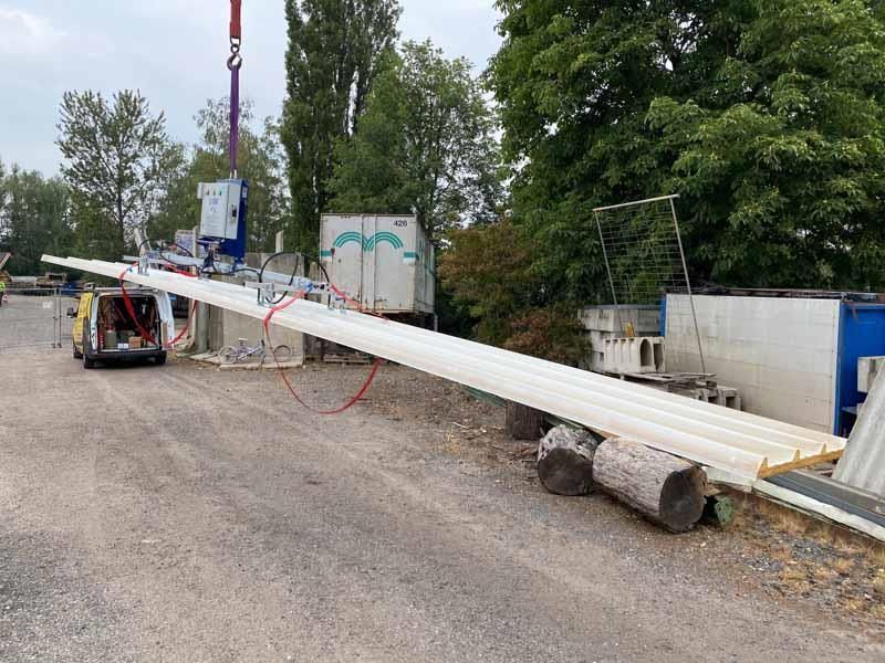 Ein großes weißes Rohr wird auf einem Parkplatz von einem Kran angehoben.