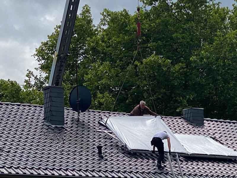 Zwei Männer installieren Solarmodule auf dem Dach eines Hauses.