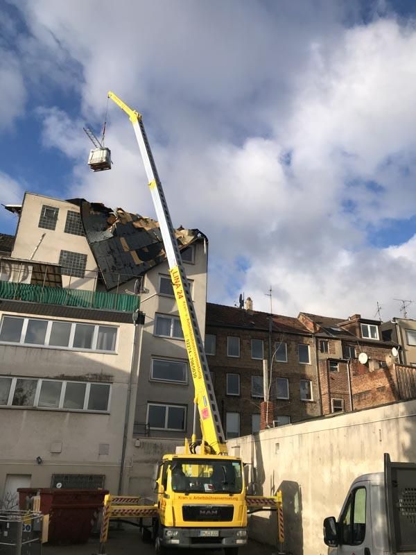 Ein gelber LKW mit einem daran befestigten Kran steht vor einem Gebäude
