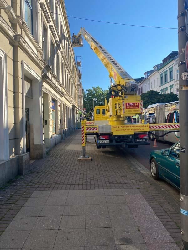 Ein gelber LKW mit einem Kran auf der Rückseite steht auf einem Bürgersteig