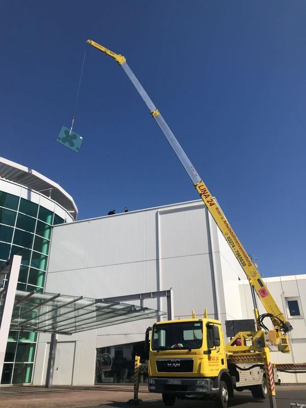 Ein gelber LKW mit einem daran befestigten Kran steht vor einem Gebäude