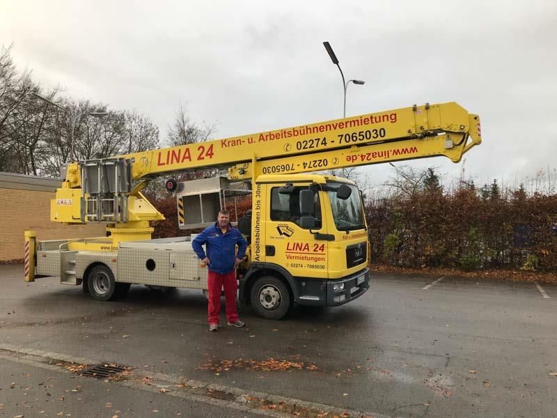 Ein Mann steht vor einem gelben Lina 24 LKW