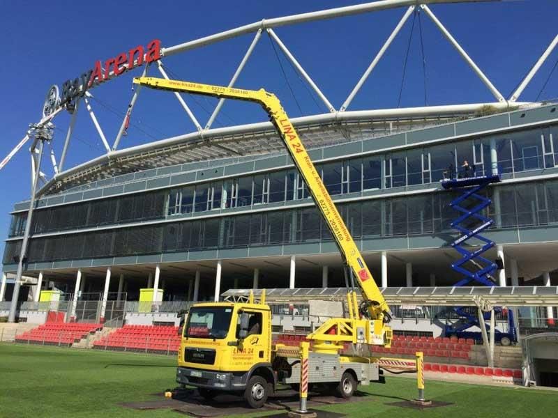 Ein gelber LKW steht vor einem großen Gebäude mit der Aufschrift Arena