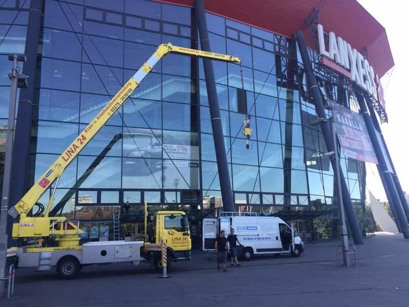 Ein gelber Lastwagen mit einem daran befestigten Kran steht vor einem großen Gebäude.