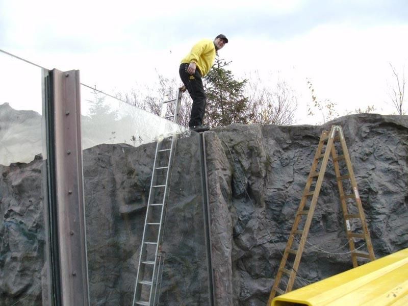 Ein Mann in einem gelben Hemd steht mit einer Leiter auf einem Felsen