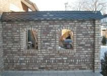 Eine Backsteinmauer mit zwei Fenstern und einem Dach.