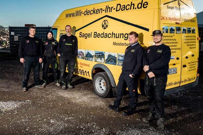 Eine Gruppe Männer steht vor einem gelben Lieferwagen.