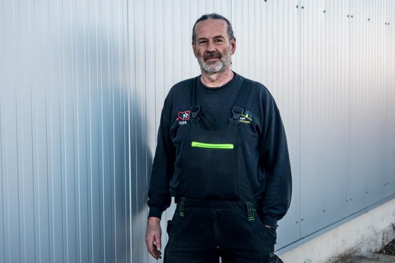 Ein Mann im Overall steht vor einer Wand.