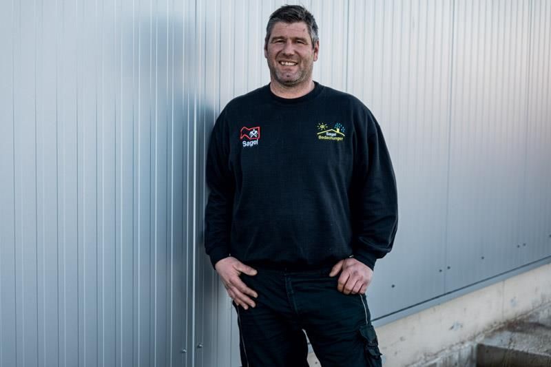 Ein Mann steht mit den Händen in den Taschen vor einer Wand.